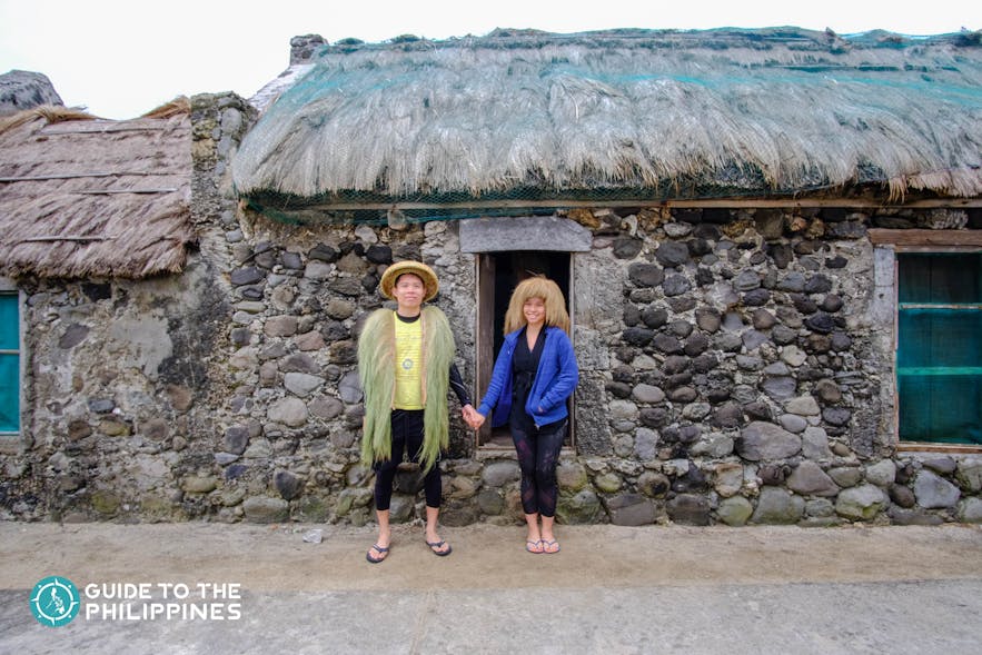 Happy couple travelers wearing native attire in front of a stone house