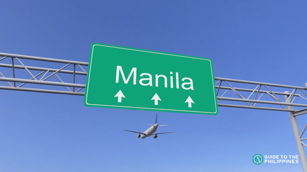 A plane flying over a signage of Manila near the airport