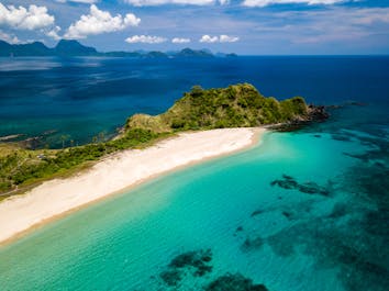Aerial drone view of an empty, beautiful tropical beach surrounded by coral reef and greenery (Nacpan Beach, Palawan)